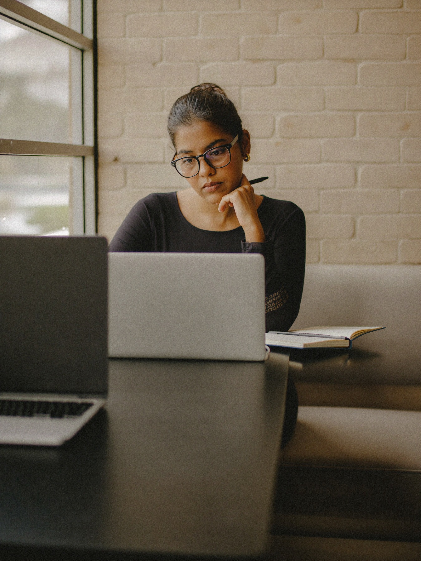 A woman thinking at a cafe table with a laptop