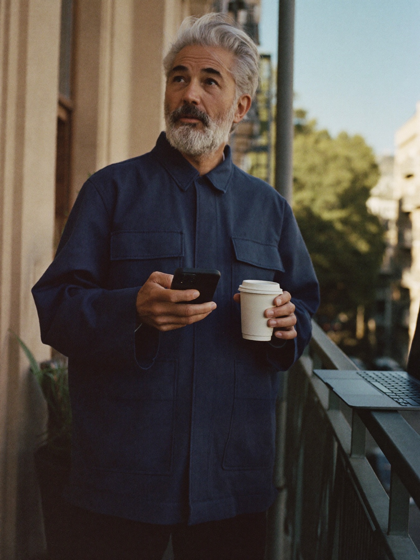 A man on a balcony with coffee and his phone